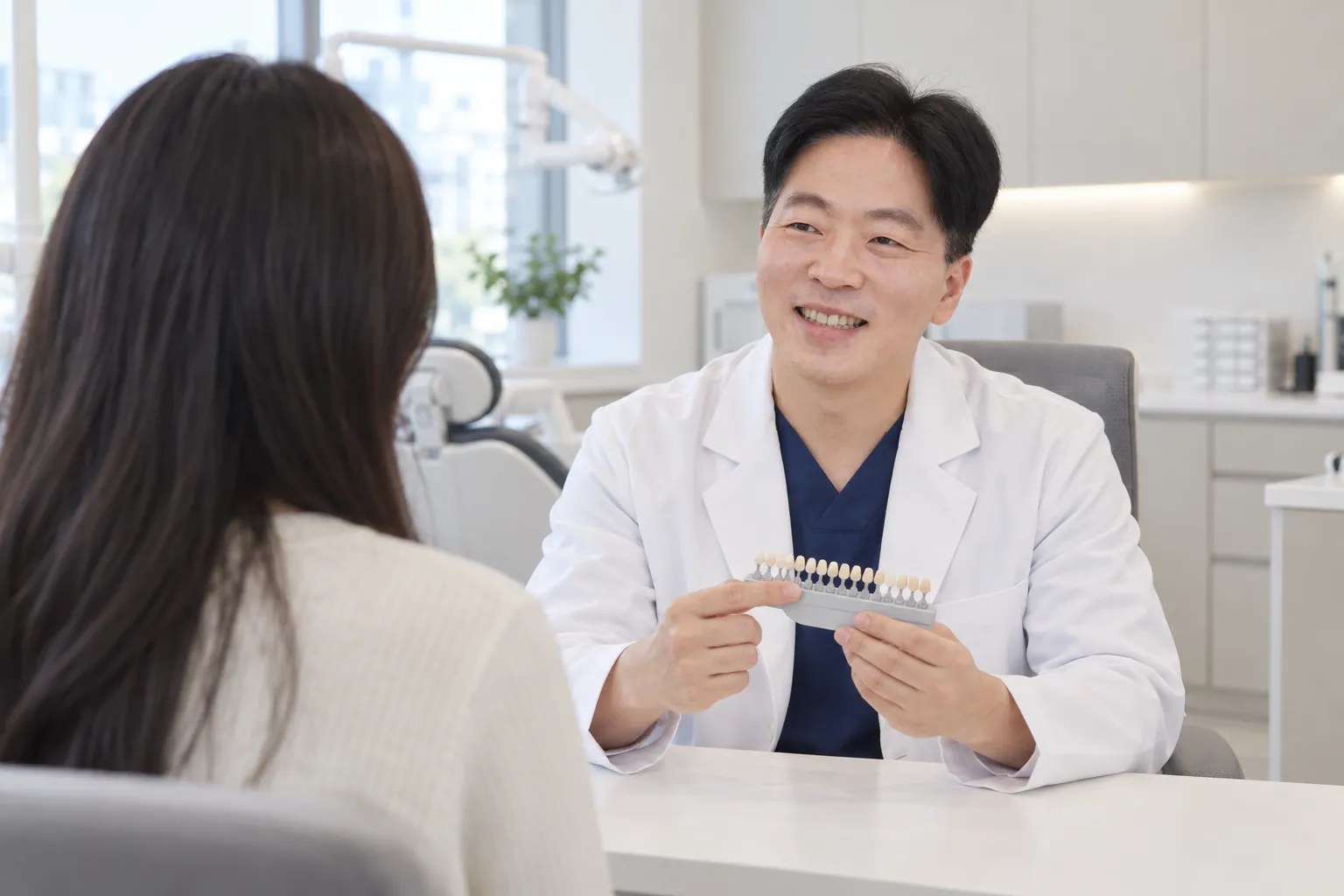 상담실에서 한정길 대표원장이 치아 색상 비교표를 보여 주며 내원객과 이야기를 나누는 모습을 표현한 연출 이미지(AI 제작)
